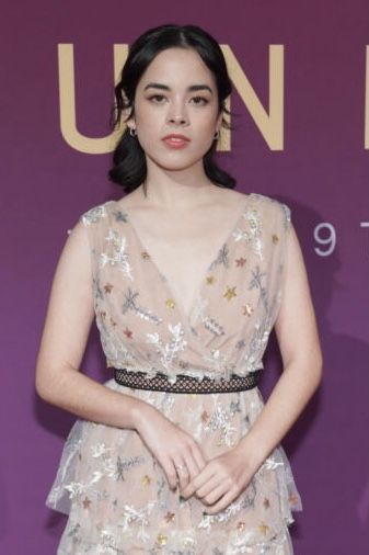 a woman standing in front of a purple wall wearing a dress with flowers on it