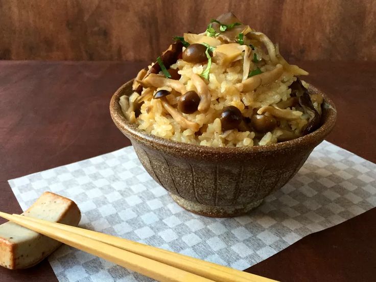 a brown bowl filled with rice and vegetables next to chopsticks on top of a table