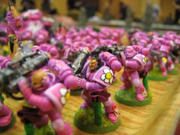 some pink warhammers are lined up on a table with people in the background