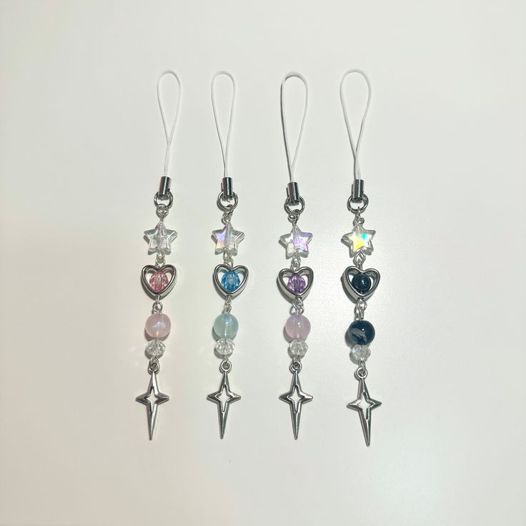 four different colored charms are hanging from silver earwires on a white surface, one has a star and the other has a heart