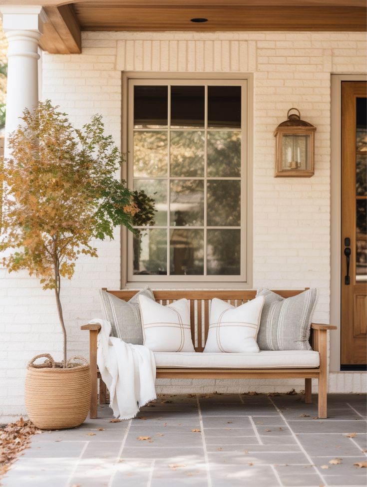 a wooden bench sitting in front of a white brick house next to a potted tree