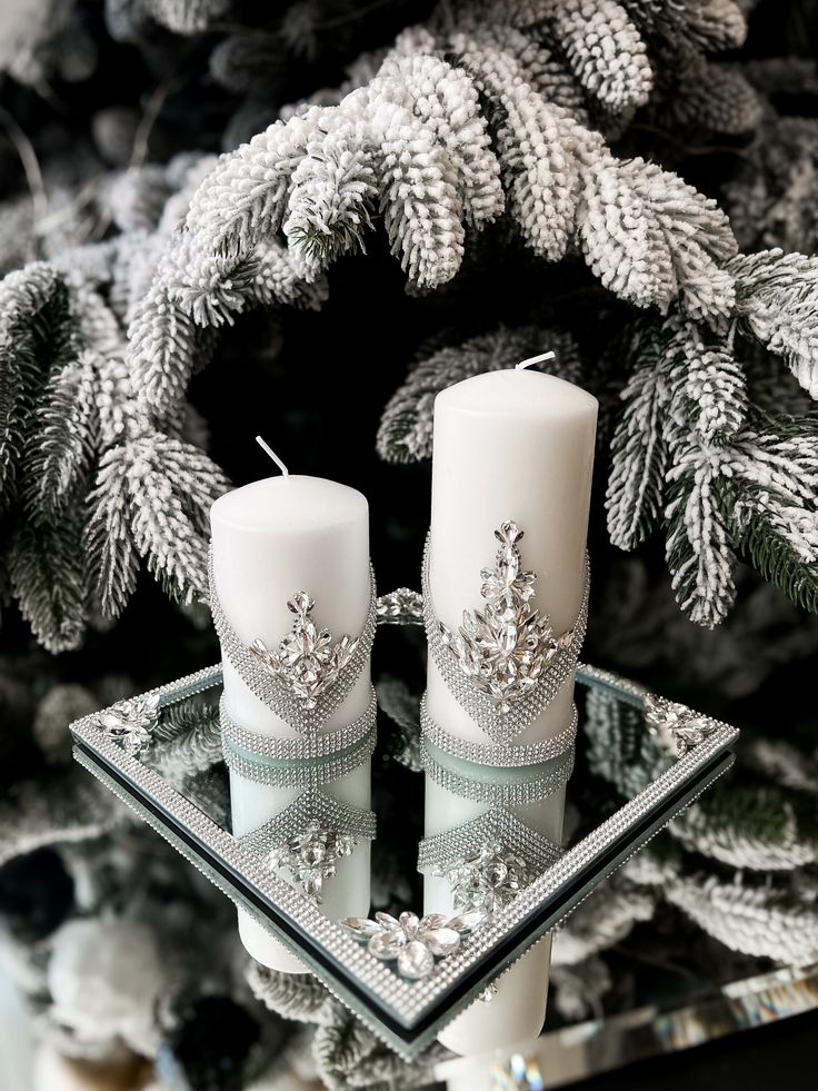 two white candles sitting on top of a glass tray next to a christmas tree with pine cones