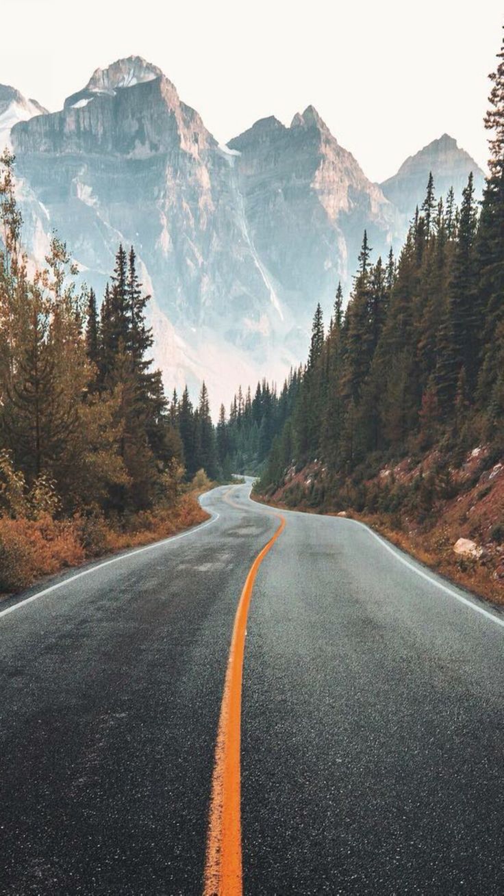 an empty road surrounded by trees and mountains