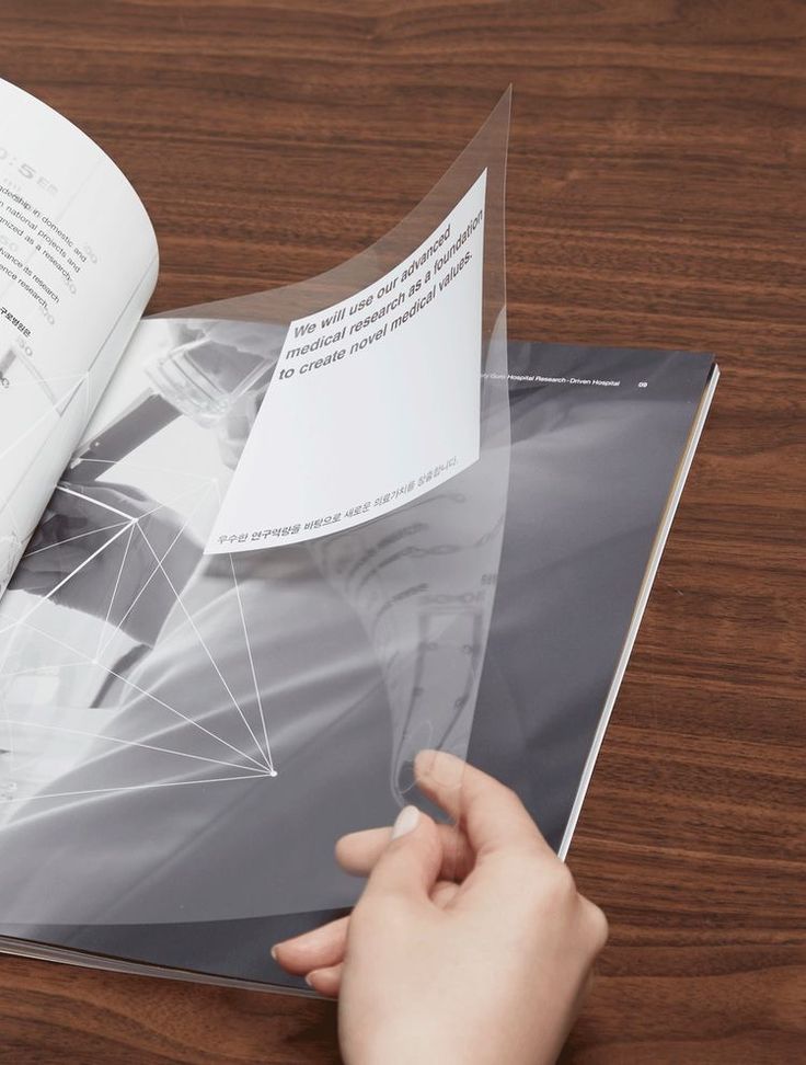 a person holding an open book on top of a wooden table