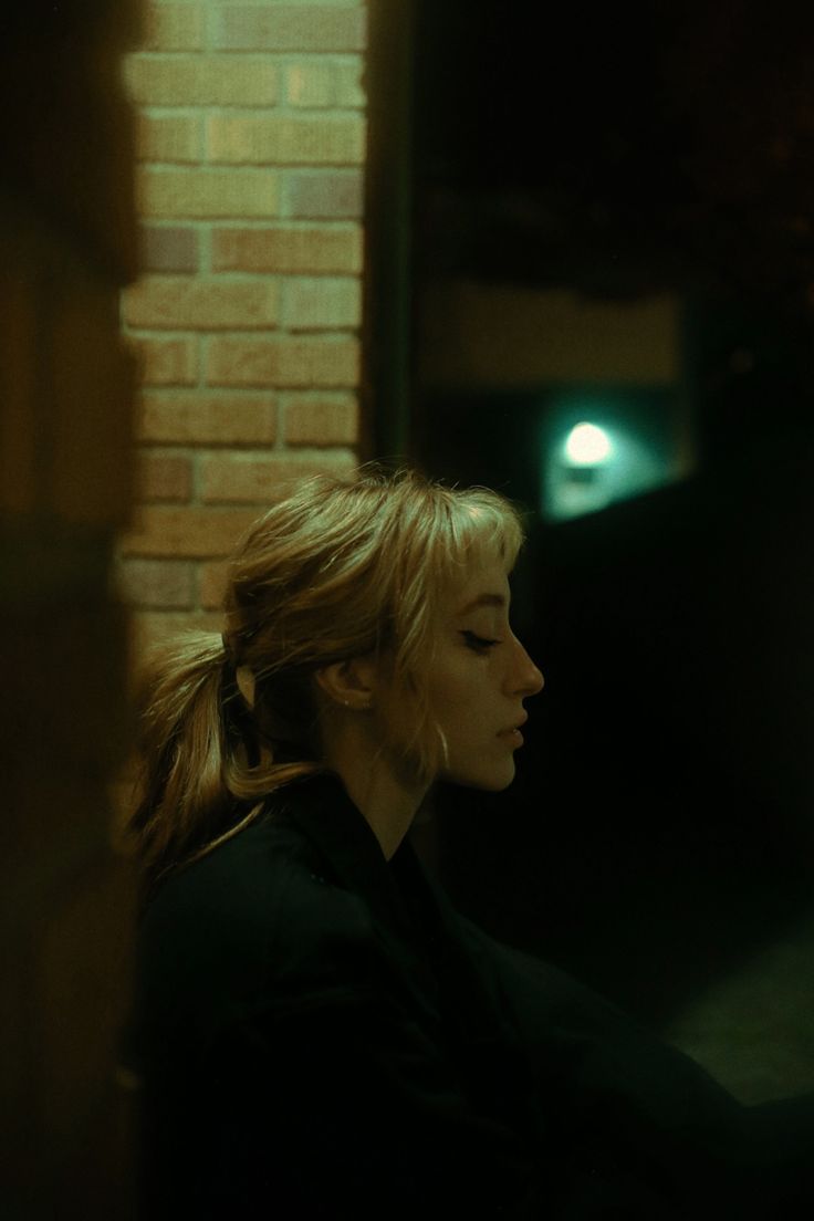 a woman sitting in front of a brick wall next to a light on the side of a building