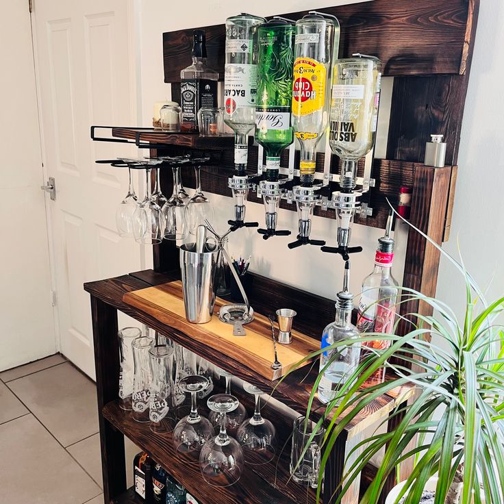 a wooden shelf filled with lots of glasses and liquor bottles next to a potted plant