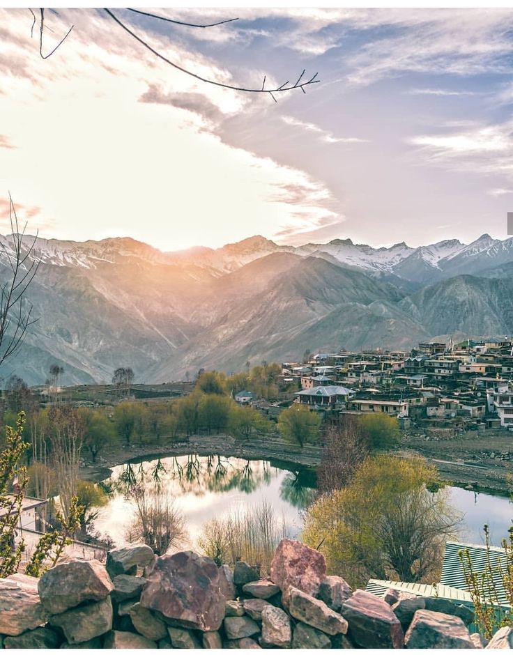 the sun shines brightly over a small town and river in front of mountains with houses on them