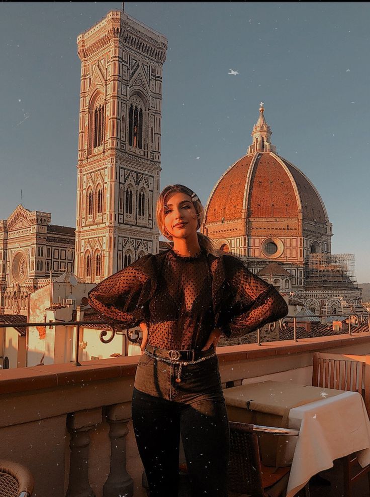 a woman standing on top of a roof next to a tall building with a clock tower in the background