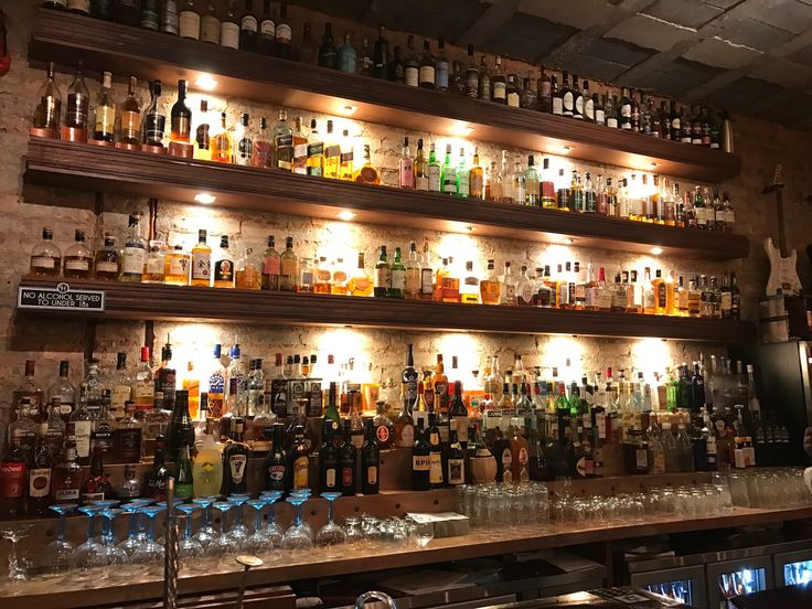 a bar with many bottles and glasses on the shelves above it, all lit up at night