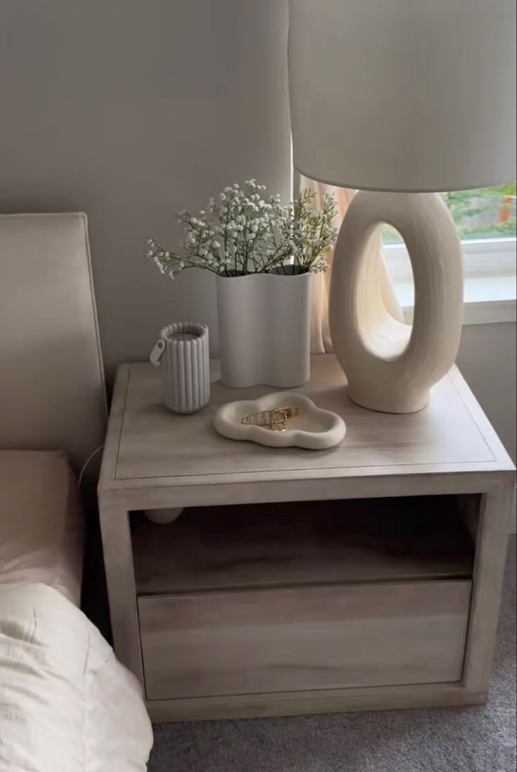 a table with a lamp and vase on it next to a bed in a room