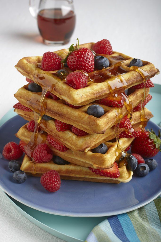 a stack of waffles with syrup and berries on a blue plate next to a glass of tea