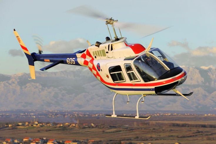 a red, white and blue helicopter flying in the air with mountains in the background