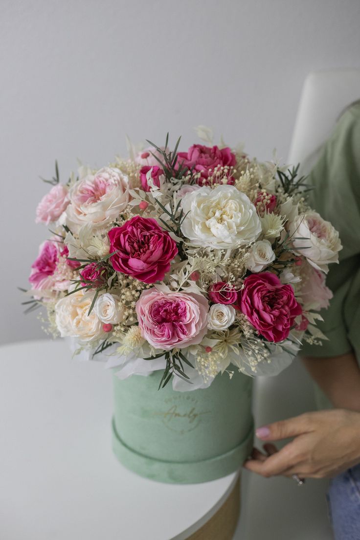 a woman holding a bouquet of flowers on top of a white table next to a green bucket