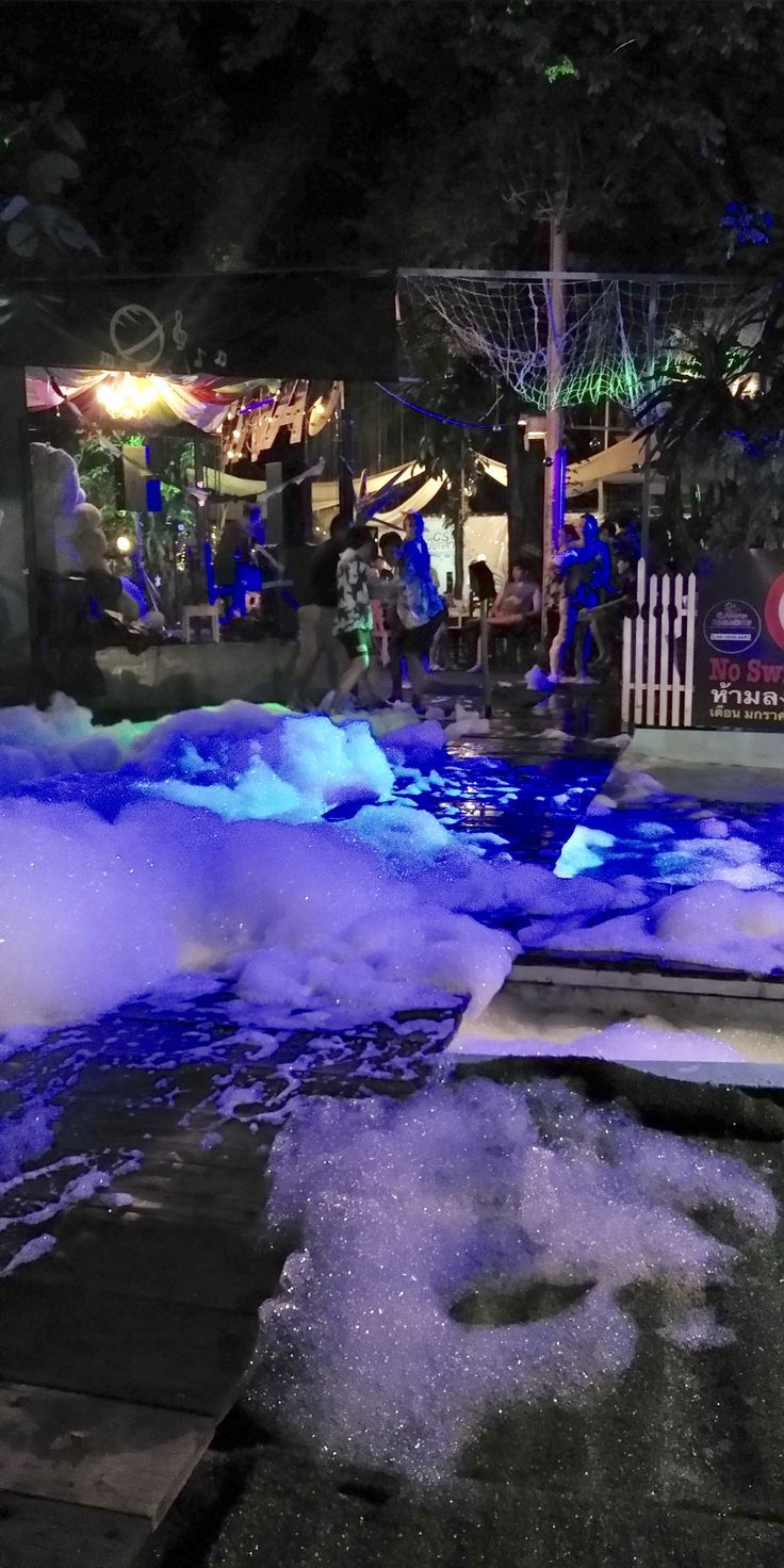 the water is blue and foamy in the pool at night time, with people standing around