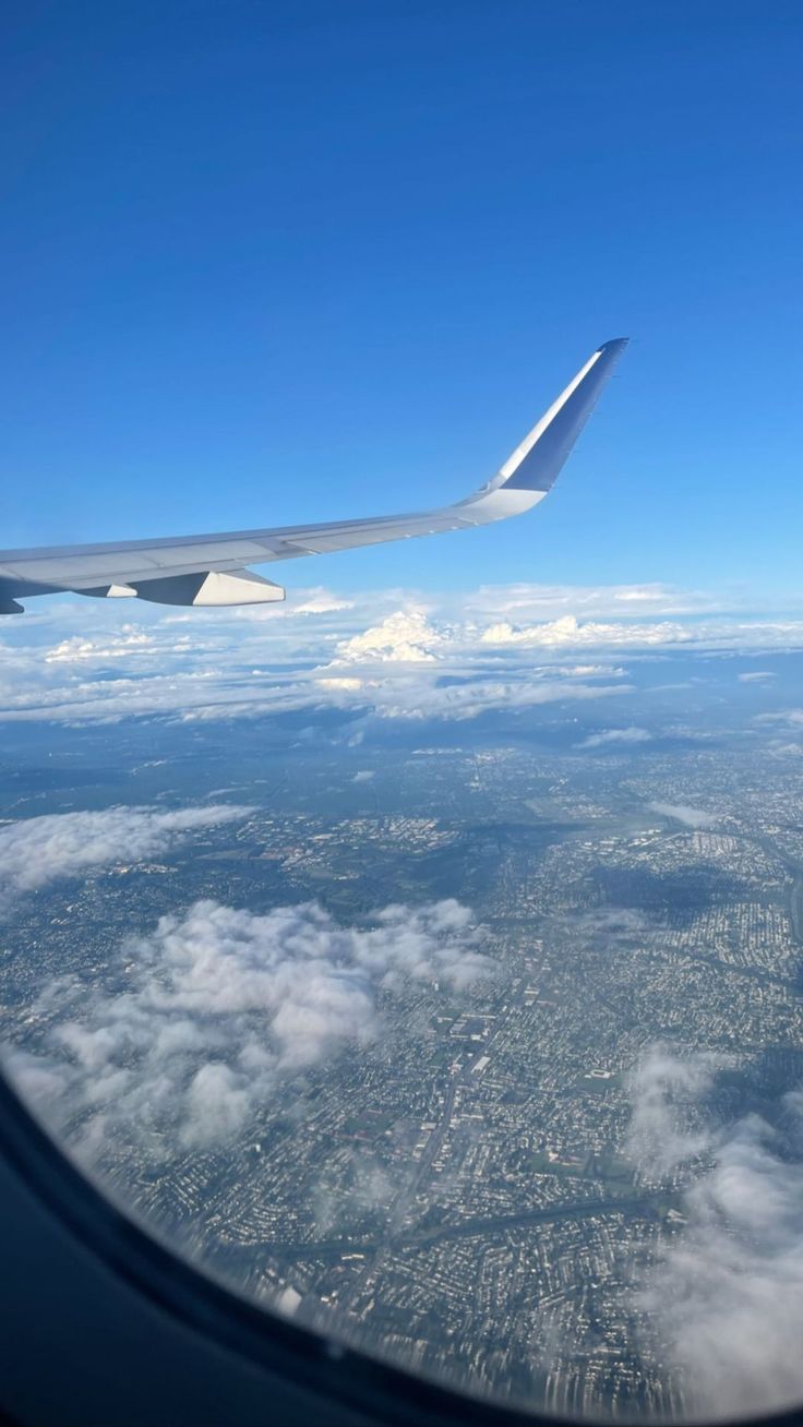 the wing of an airplane as seen from above in the sky with clouds and land below