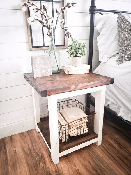 a white bed with a wooden table next to it and a basket on the side