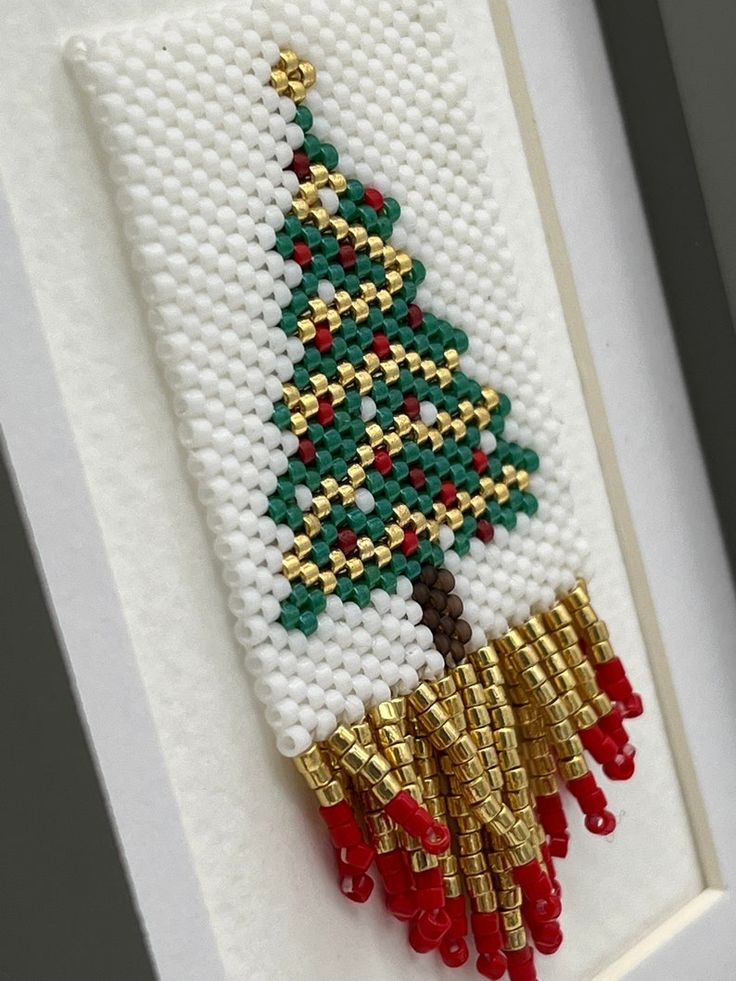 a cross stitch christmas tree hanging on a white framed frame with red and green beads