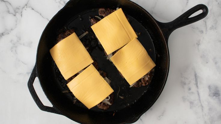 four pieces of cheese sitting in a skillet on top of a marble countertop