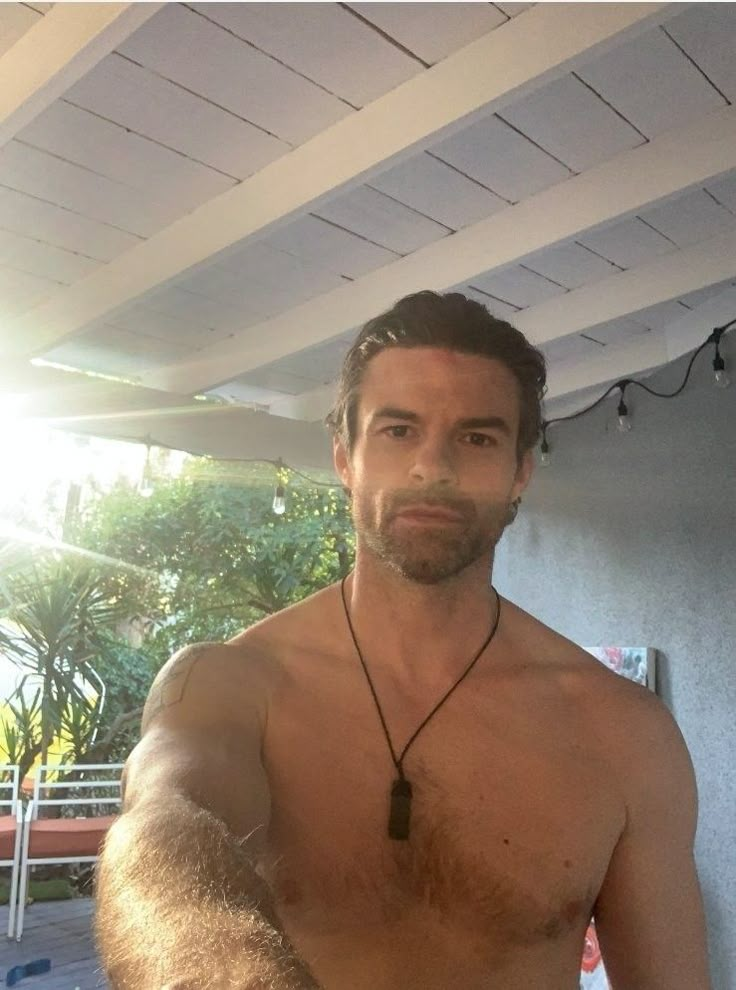 a man with no shirt on standing in front of a pool and wearing a necklace