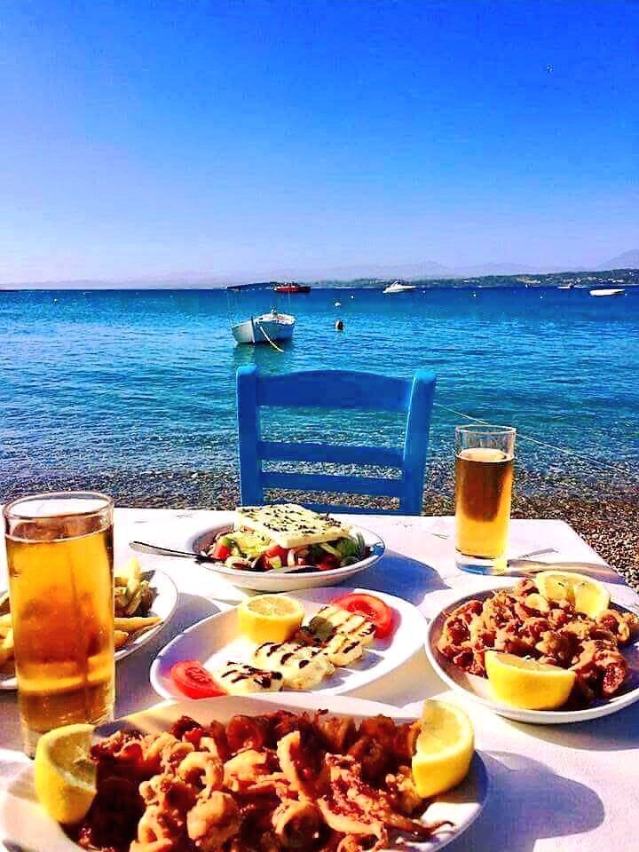 a table with plates of food and drinks on it near the water's edge