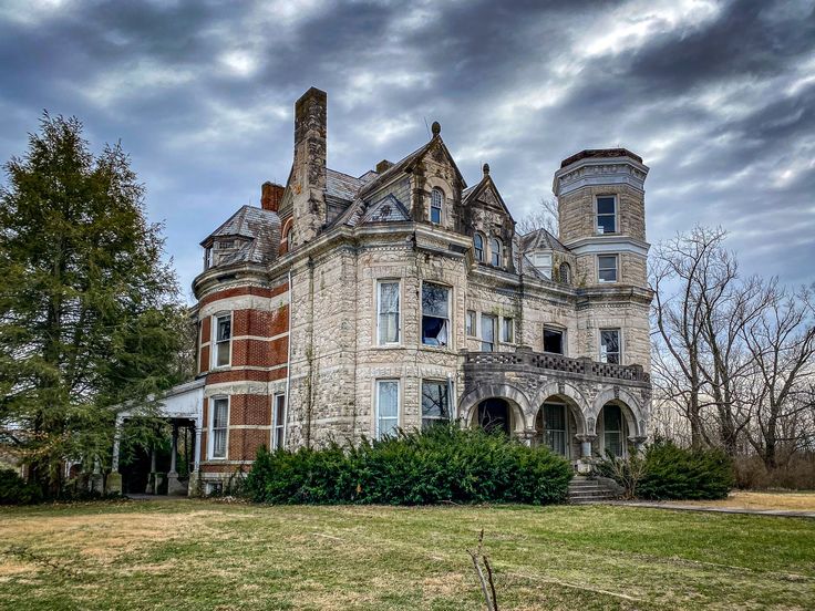 an old brick and stone house in the middle of a grassy area with trees on either side