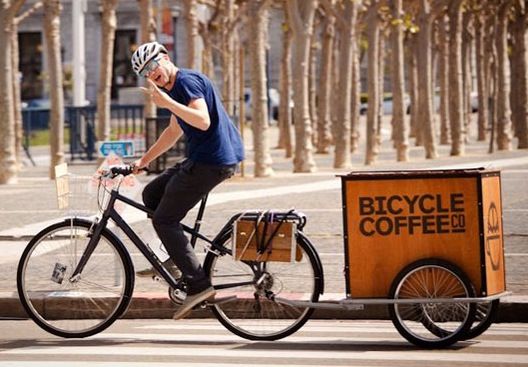 a man riding a bike next to a coffee box