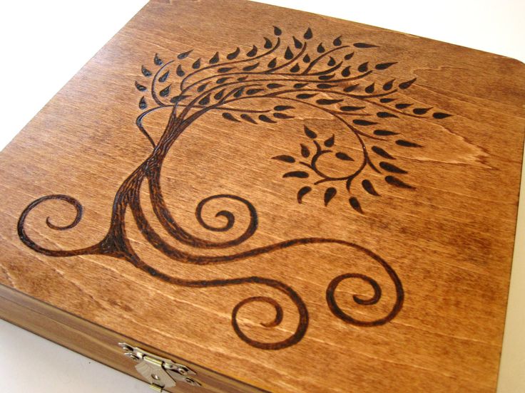 a wooden box with a tree on the inside and swirls in the outside, sitting on a white surface