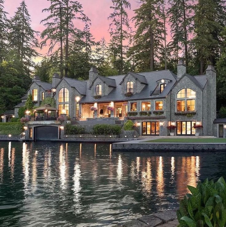 a large house sitting on top of a lake next to a lush green forest covered hillside