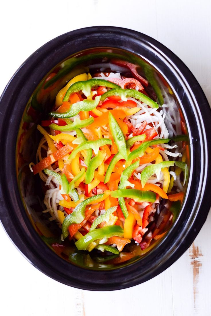 a black bowl filled with vegetables on top of a white table