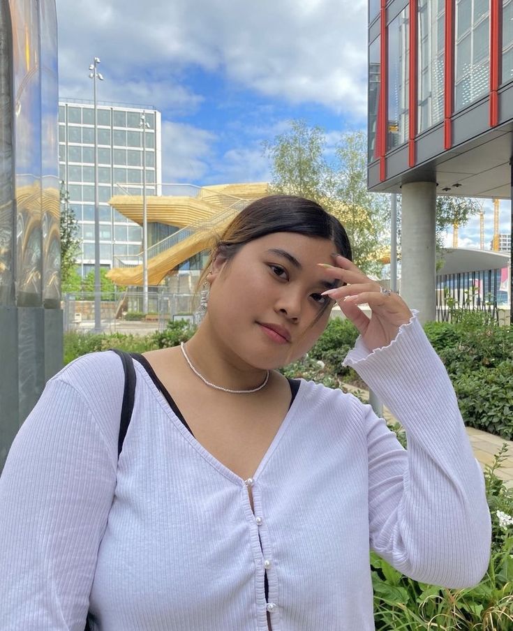 a woman standing in front of a building holding her hand to her face and looking at the camera