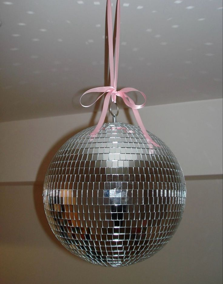 a mirror ball hanging from the ceiling with a pink ribbon on it's end