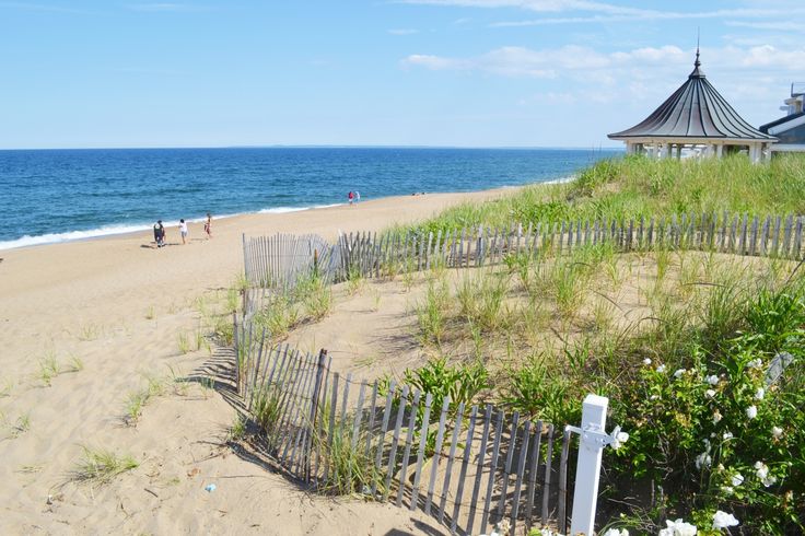 a beach with people walking on the sand and water in the background, near a wooden fence