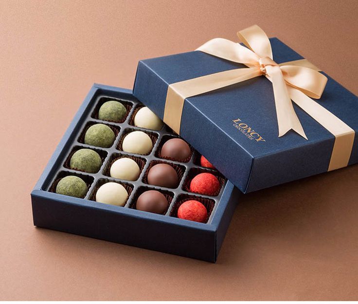 a blue box filled with assorted chocolates on top of a brown table next to a white ribbon