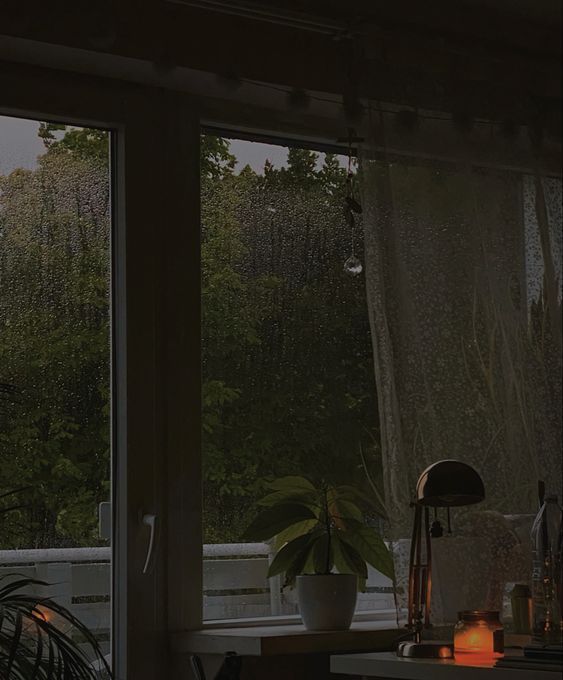 an open window with rain coming in to the yard and trees outside at night time