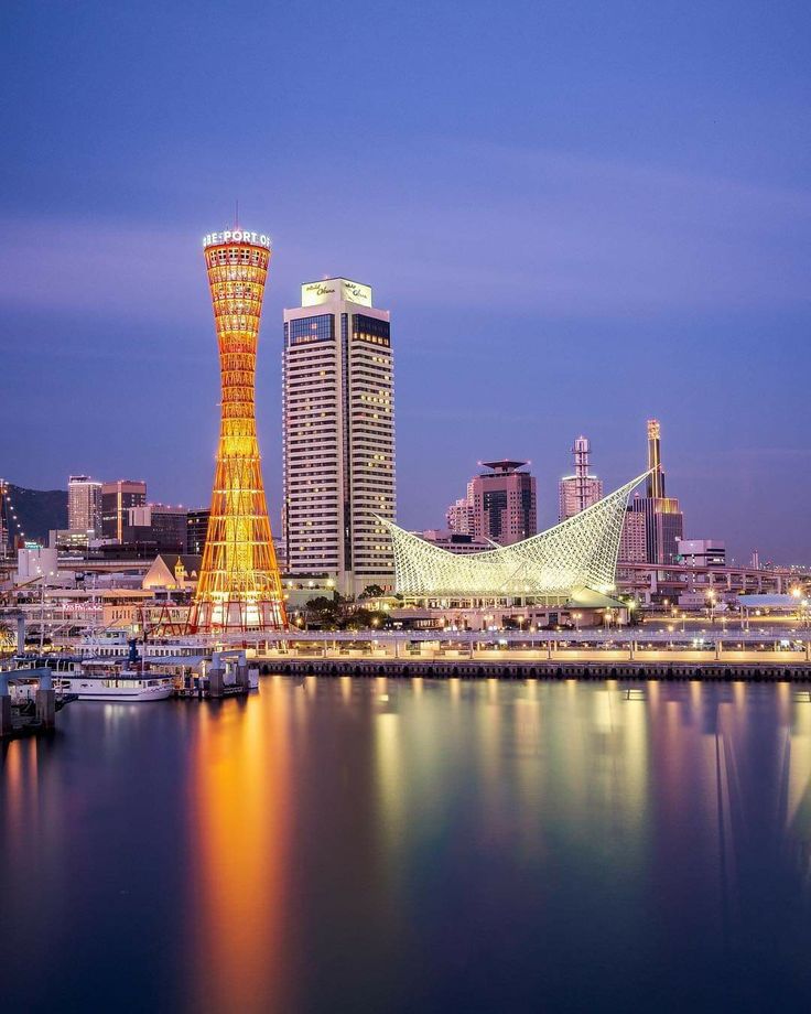 the city is lit up at night with lights reflecting on the water and boats in the harbor