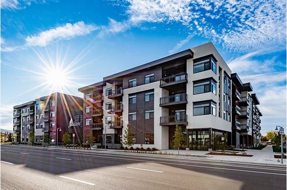 the sun shines brightly over an apartment building on a street in front of a blue sky with white clouds