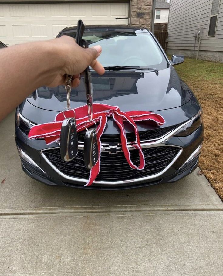 a person holding a car key in front of a black car with a red ribbon tied around it