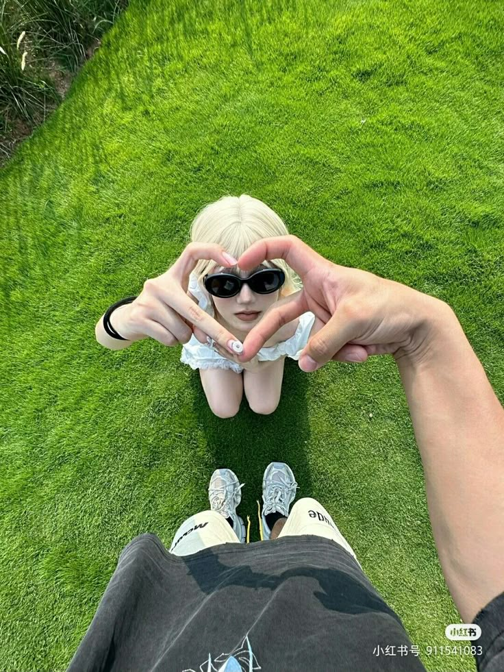 a person sitting in the grass making a heart with their hands