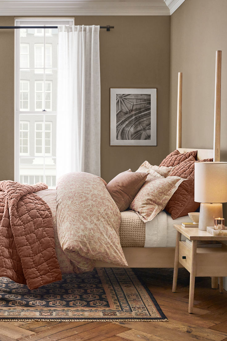 a bed sitting in a bedroom next to a window covered in pink and brown blankets