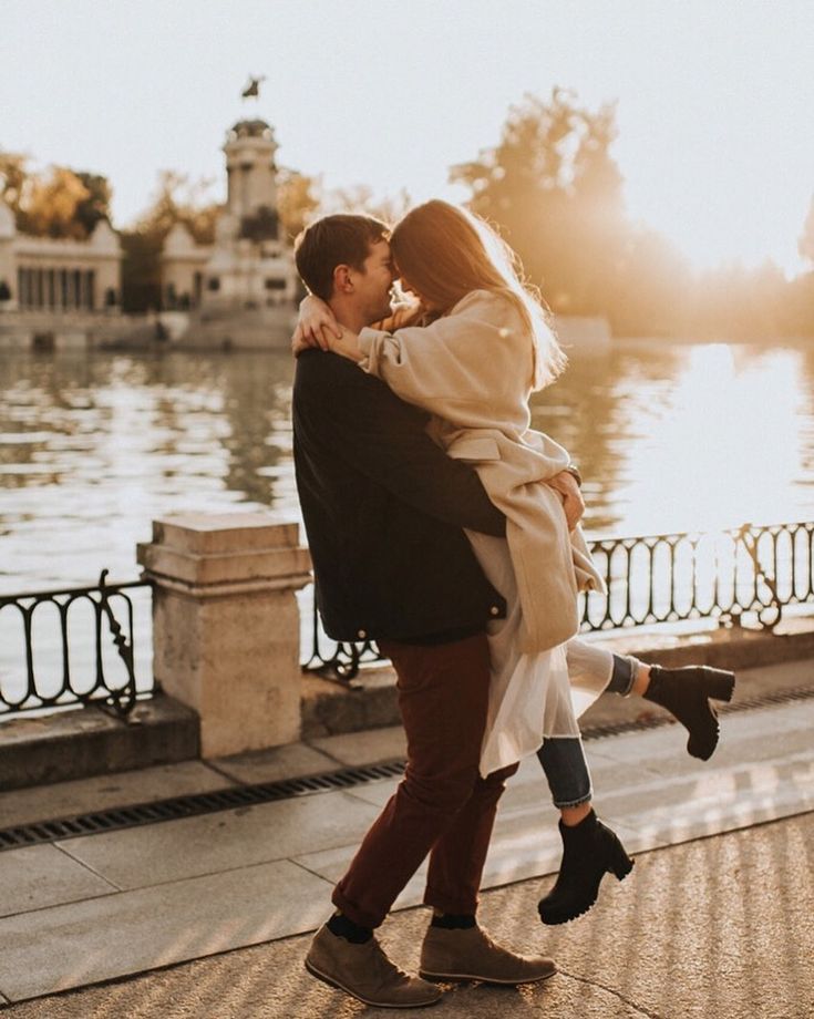 a man and woman are walking by the water in front of some buildings with their arms around each other