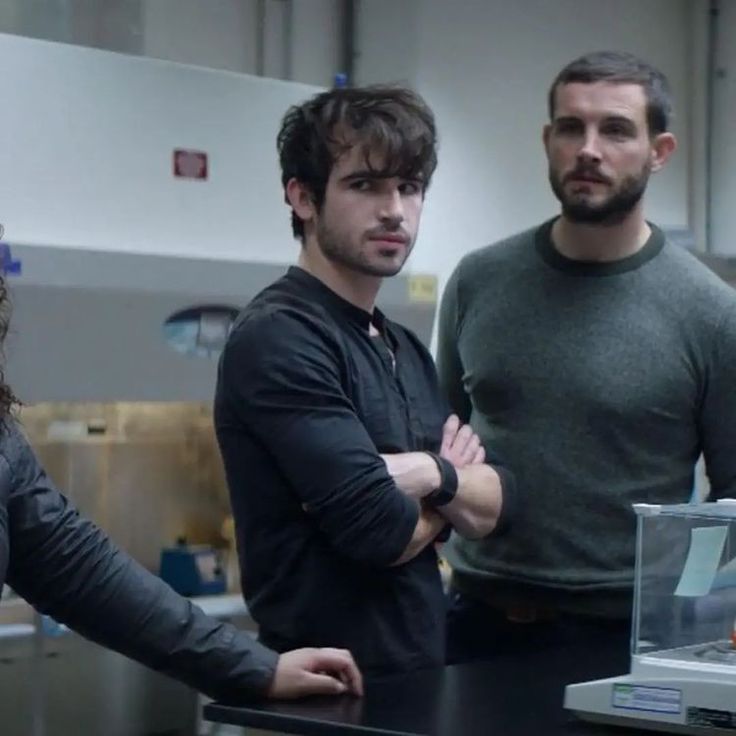 two men and a woman standing in front of a table with an object on it