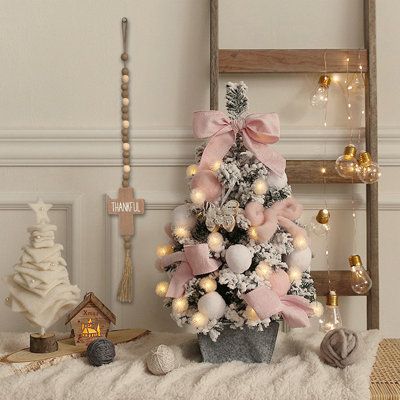 a small christmas tree with pink and white ornaments in a pot next to a ladder