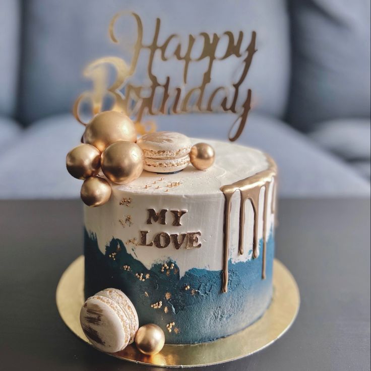 a birthday cake decorated with gold and blue icing is on a table next to a couch