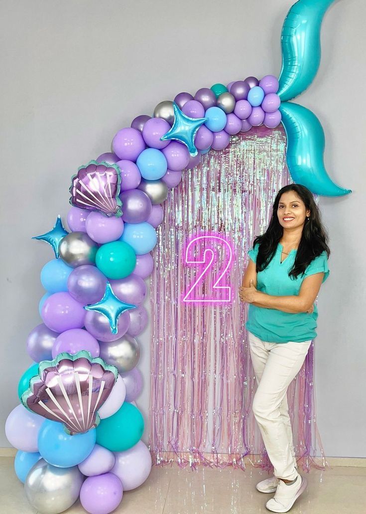 a woman standing in front of a balloon arch with mermaid tail decorations and balloons on it