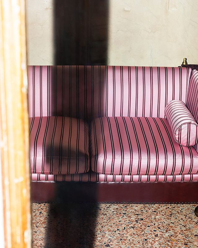 a pink striped couch sitting on top of a floor next to a wall with a mirror