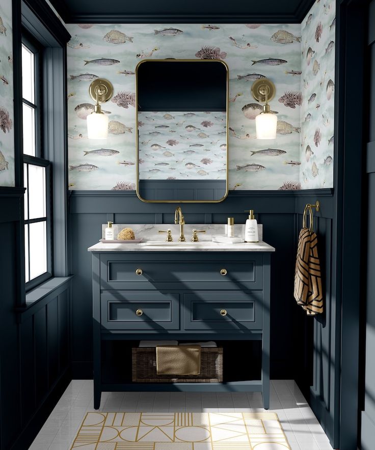 a bathroom with blue cabinets and wallpaper on the walls, along with a gold framed mirror