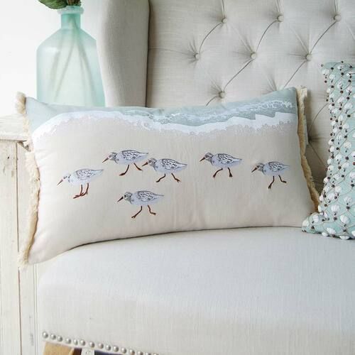 a white chair with a blue vase on top of it next to a pillow that has birds embroidered on it