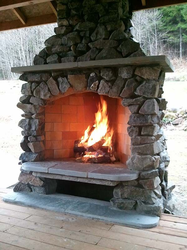 an outdoor fireplace with rocks on the outside and fire in the inside, as well as wood