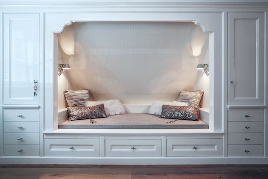 a room with some white cabinets and pillows on top of the bed, in front of it is a built - in bench