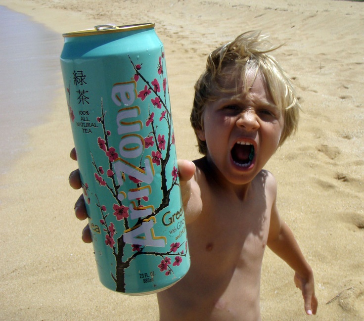 a young boy holding up a can of soda on the beach